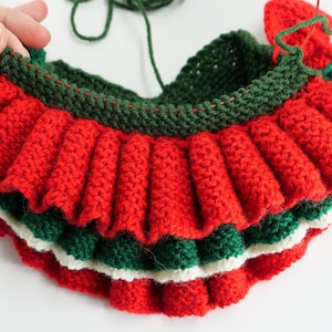 K&ouml;nnte beinhalten: Nahaufnahme eines gestrickten Weihnachtskragens in Arbeit. Der Kragen hat Schichten aus rotem, gr&uuml;nem und wei&szlig;em Garn mit einem R&uuml;schendesign. Die oberste Schicht ist gr&uuml;n, gefolgt von rot, wei&szlig; und einer weiteren gr&uuml;nen Schicht.