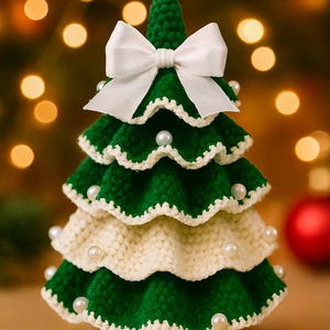 May include: A handcrafted, crochet Christmas tree in green and cream colors, adorned with white pearls and a white bow. The tree has a tiered design and is a festive holiday decoration.