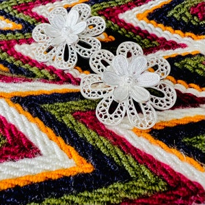 Puede incluir: Dos pendientes de plata en forma de flor con filigrana sobre un fondo de tela a rayas de colores.