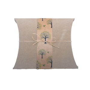 Peut inclure: Une boîte cadeau en carton brun avec une bande de papier décorative représentant des arbres verts et des oiseaux. La boîte est attachée avec un nœud en ficelle naturelle.