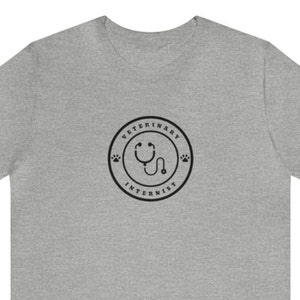 Könnte beinhalten: Graues T-Shirt mit kurzen Ärmeln und einem schwarz-weißen Grafikdruck eines Stethoskops in einem Kreis mit dem Text "Veterinary Internist" um den Kreis herum.