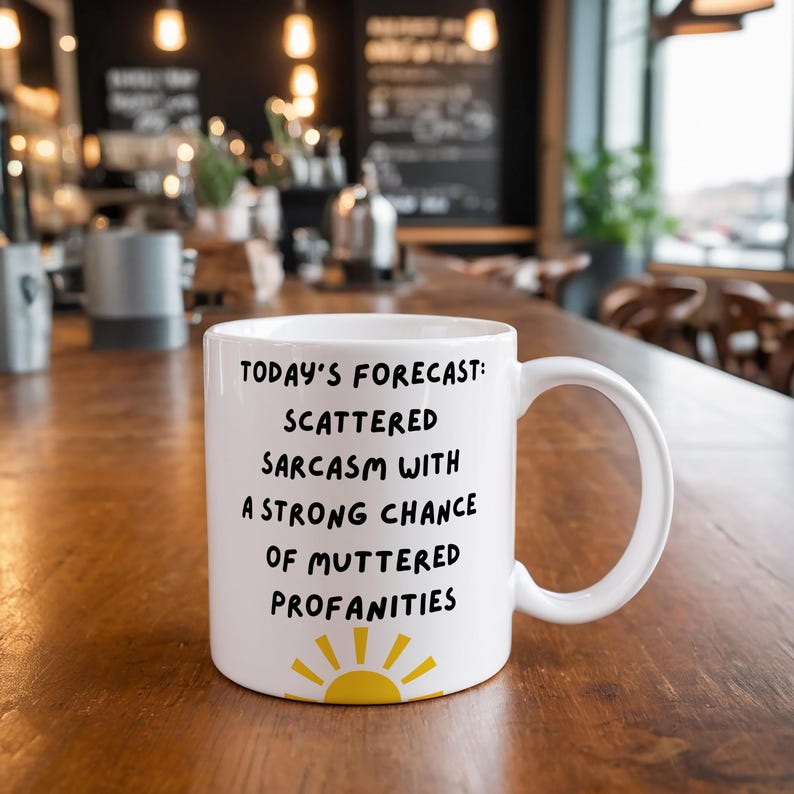 May include: White ceramic mug with a black sun graphic and the text "TODAY'S FORECAST: SCATTERED SARCASM WITH A STRONG CHANCE OF MUTTERED PROFANITIES".