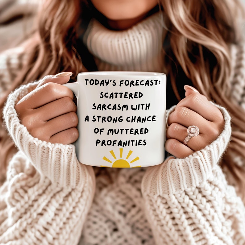 May include: White ceramic mug with a black and yellow sun graphic and the text "TODAY'S FORECAST: SCATTERED SARCASM WITH A STRONG CHANCE OF MUTTERED PROFANITIES".