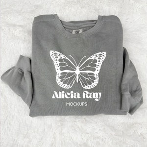以下が含まれることがあります： 白い蝶のグラフィックと「Alicia Ray MOCKUPS」の文字が前面に印刷されたグレーのトレーナー