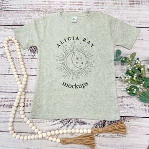 May include: A light green short-sleeved t-shirt with the text "Alicia Ray" and a moon and stars graphic. The text "mockups" is printed below the graphic.