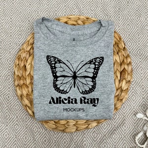 Könnte beinhalten: Graues T-Shirt mit einem schwarzen Schmetterlingsmotiv und dem Text "Alicia Ray Mockups".