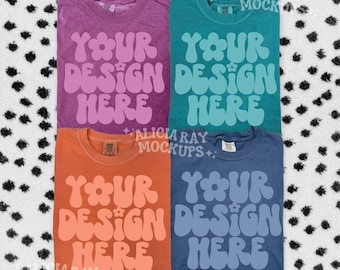 May include: Four t-shirts in shades of purple, teal, orange, and blue, each with the text "YOUR DESIGN HERE" in a retro font. The shirts are arranged on a black and white polka dot background.