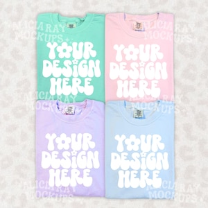 May include: Four pastel-colored t-shirts: mint green, pink, lavender, and light blue. Each shirt has the text "YOUR DESIGN HERE" in a white, retro font. The shirts are neatly folded, showcasing the potential for custom designs.
