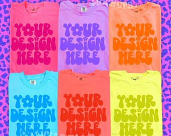 May include: Six colorful t-shirts, each folded and displaying the text "YOUR DESIGN HERE" in a retro font. The shirts are in shades of pink, purple, orange, blue, coral, and yellow. The background is a pink leopard print.