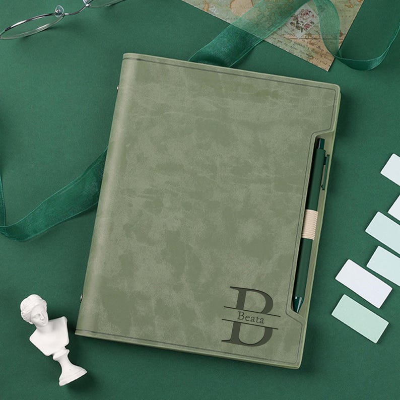 May include: A green leather-bound journal with a personalised initial "B" and the name "Beata" engraved on the front. The journal has a pen holder and a pen.