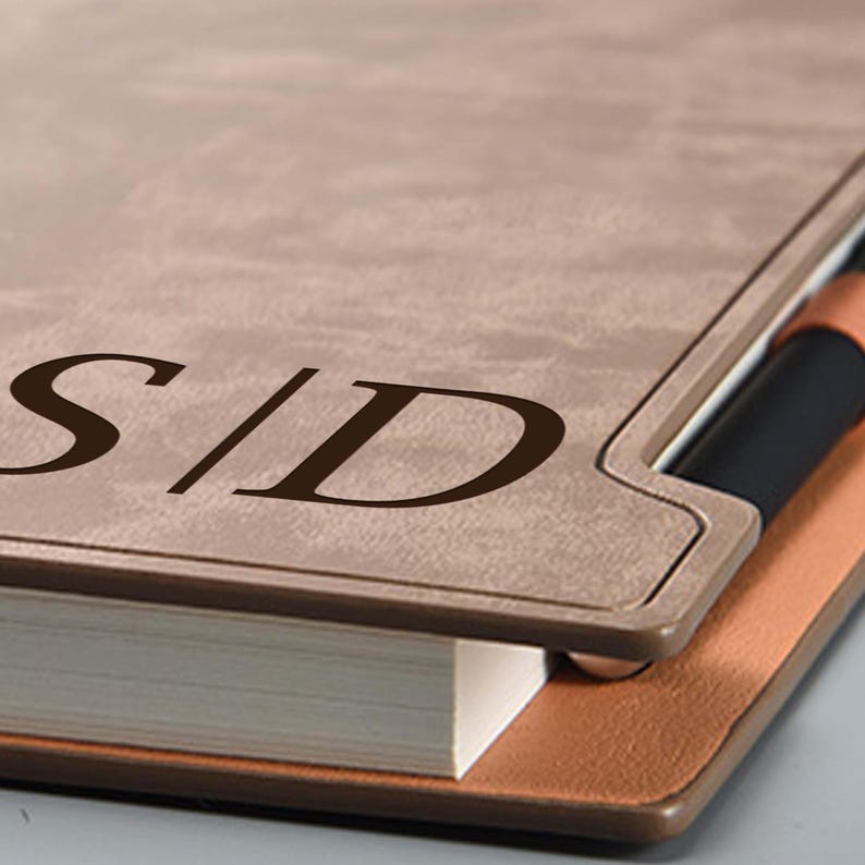 May include: A brown leather-bound journal with a pen holder and the initials "S|D" embossed on the front cover.