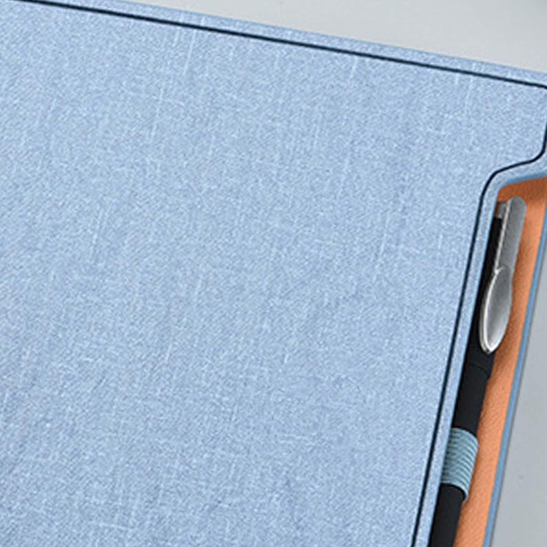 May include: A light blue notebook with a pen holder and a black pen inserted. The notebook has a textured fabric cover.