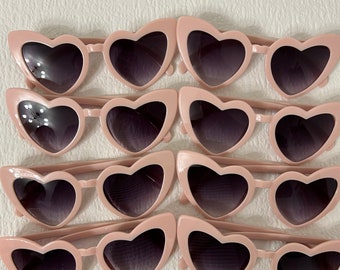 May include: Set of ten pink heart-shaped sunglasses with dark lenses. The sunglasses are arranged in four rows of two.
