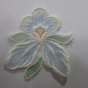 May include: A delicate blue and white embroidered flower applique with a light green stem and leaves. The flower has a white centre with a light orange centre.