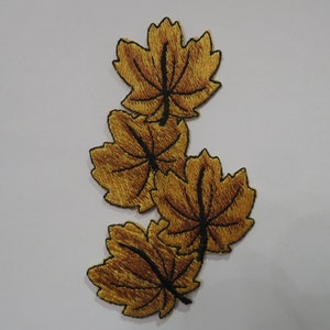 May include: Four gold embroidered maple leaves with black stitching, arranged in a vertical stack.