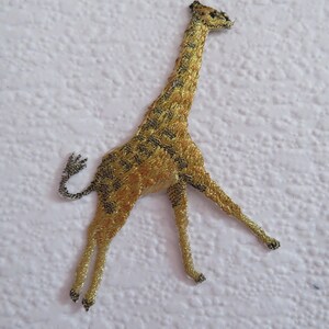 May include: A gold embroidered iron-on patch of a giraffe with a black outline. The giraffe is standing on all four legs with its head tilted to the side.