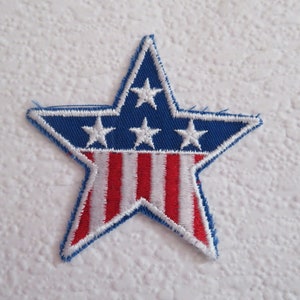 May include: A blue star-shaped patch with a red and white striped design resembling the American flag. There are five white stars on the blue portion of the patch.
