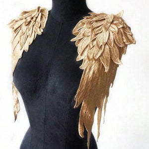 May include: A pair of gold velvet wings with a feathery design. The wings are attached to a black mannequin.