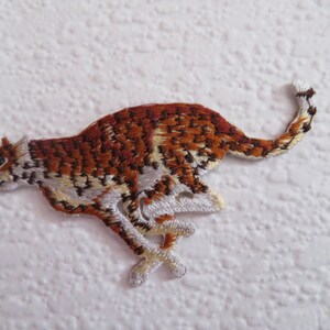 May include: Embroidered patch of a running cheetah. The cheetah is rendered in brown, orange, and white thread, showcasing detailed stitching. The patch is designed for application to fabric, ideal for clothing or accessories.