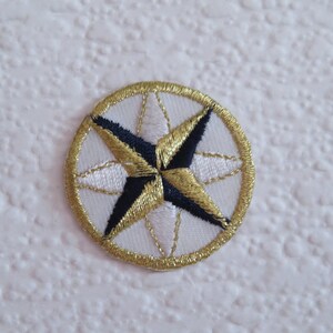May include: A white embroidered patch with a gold and black compass rose design.