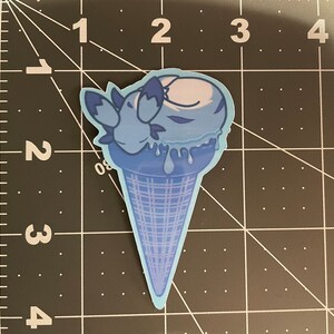 May include: A blue ice cream cone with a blue and white ice cream scoop. The ice cream is melting and dripping down the cone. The ice cream is shaped like a sleeping animal.