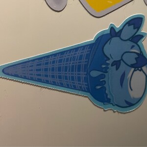 May include: A blue ice cream cone with a blue and white cartoon character on top. The ice cream is melting and dripping down the cone.