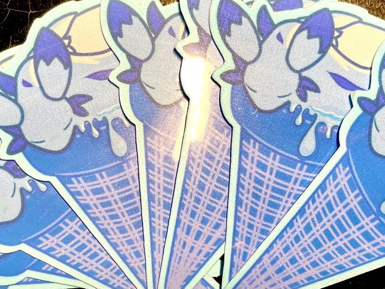 May include: A set of blue and white ice cream cone stickers with a cartoon character design. The character is a blue creature with a white face and purple eyes. The ice cream is dripping down the cone.