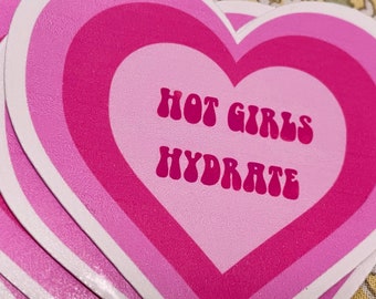 Può includere: Adesivo rosa a forma di cuore con il testo "Hot Girls Hydrate" in un font retrò.