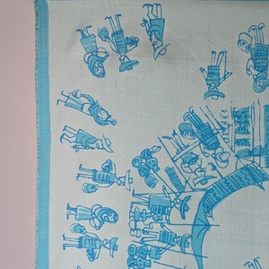 May include: A light blue silk scarf with a white background and a pattern of blue stick figures. The figures are dressed in traditional clothing and are holding various items, such as baskets and musical instruments. The scarf has a blue border.