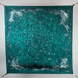 May include: A teal blue square scarf with a white and teal abstract pattern of swirling circles. The scarf has a white border and the signature "V.M.A." in the bottom right corner.