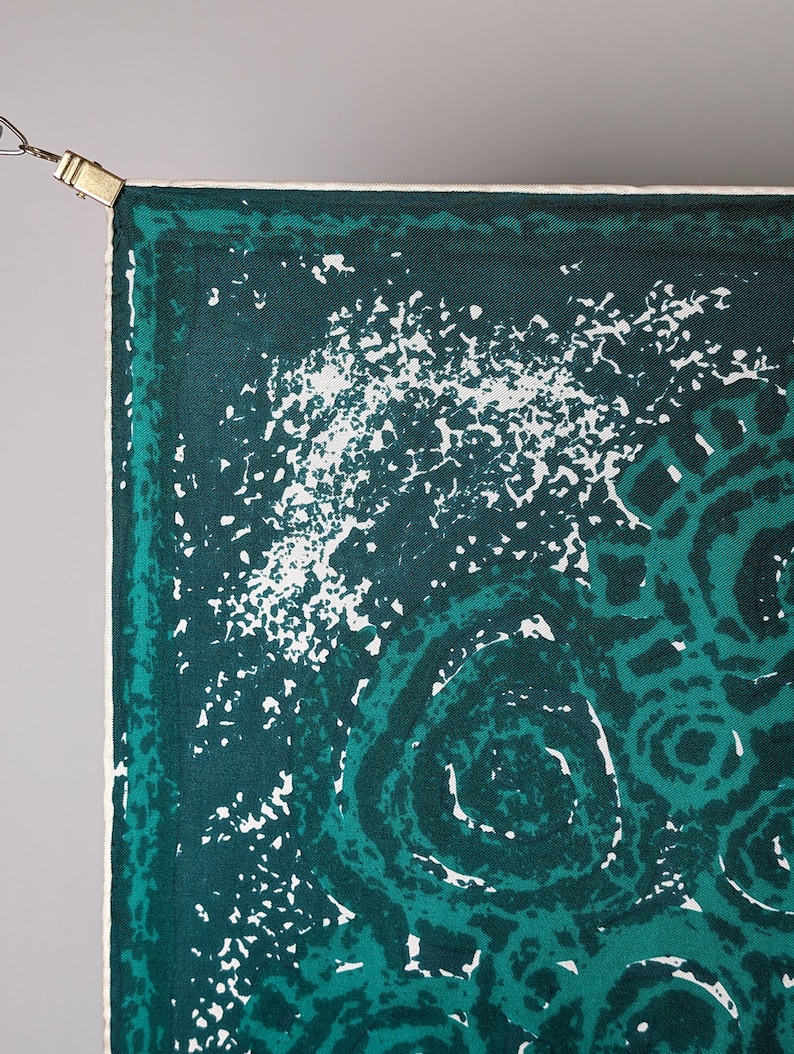 May include: A green and white patterned fabric with a white border. The fabric has a swirling pattern with white spots on a dark green background.