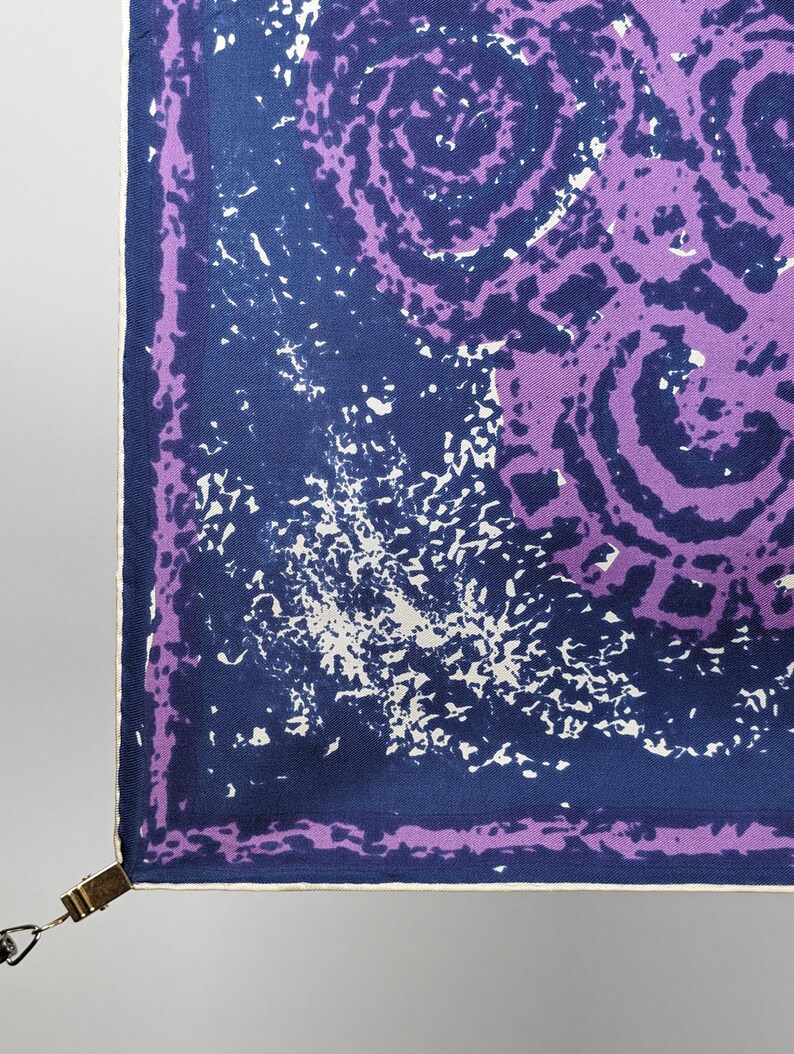 May include: A square purple and blue patterned fabric with a white border. The fabric has a swirling pattern with a white splatter effect.