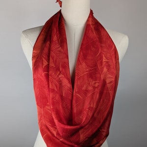 May include: A red silk scarf with a leaf pattern. The scarf is tied around a mannequin's neck.