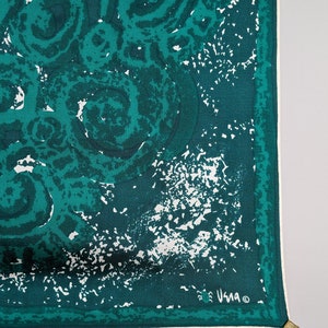 May include: A teal blue silk scarf with a white abstract pattern. The scarf has a white border and the word "Usma" is printed in the bottom right corner.