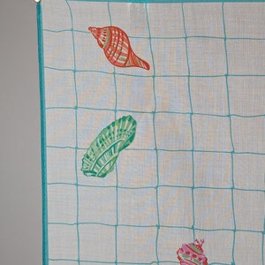 Op de afbeelding: Een wit katoenen zakdoek met een turquoise blauwe rand en een rasterpatroon. De zakdoek heeft drie kleurrijke schelpen in verschillende ontwerpen.