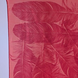 May include: A red silk scarf with a pattern of white feathers. The scarf is folded and draped over a surface.