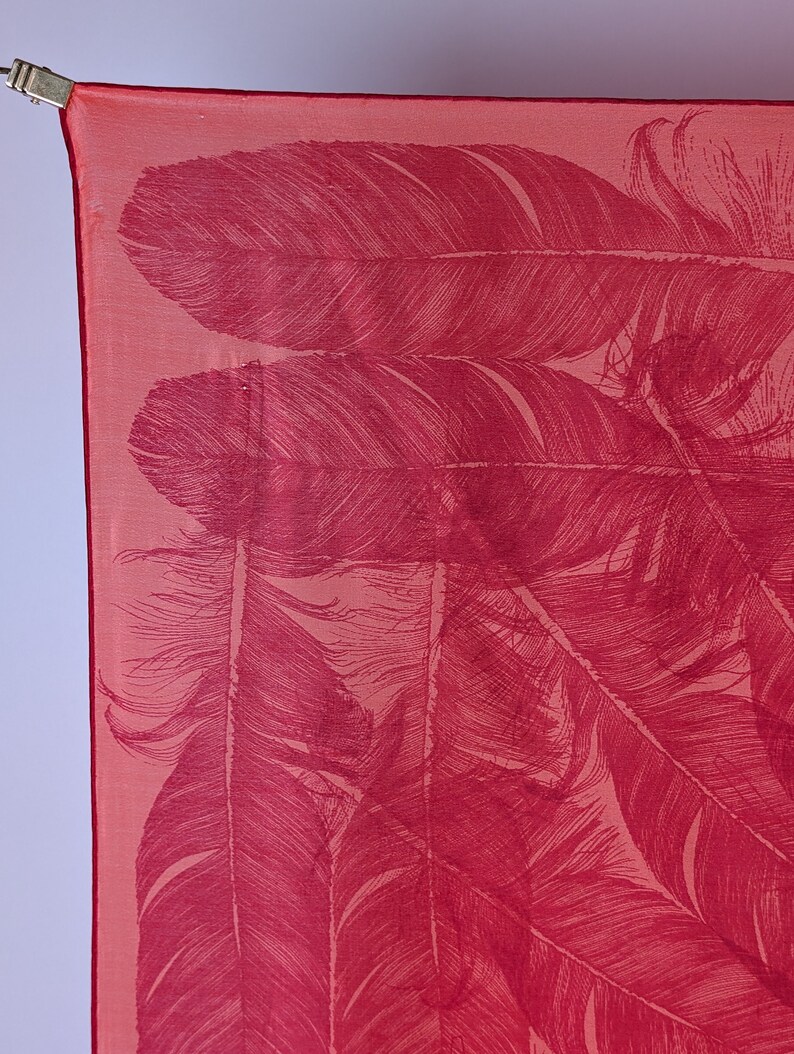 May include: A red silk scarf with a pattern of white feathers. The scarf is folded and draped over a surface.