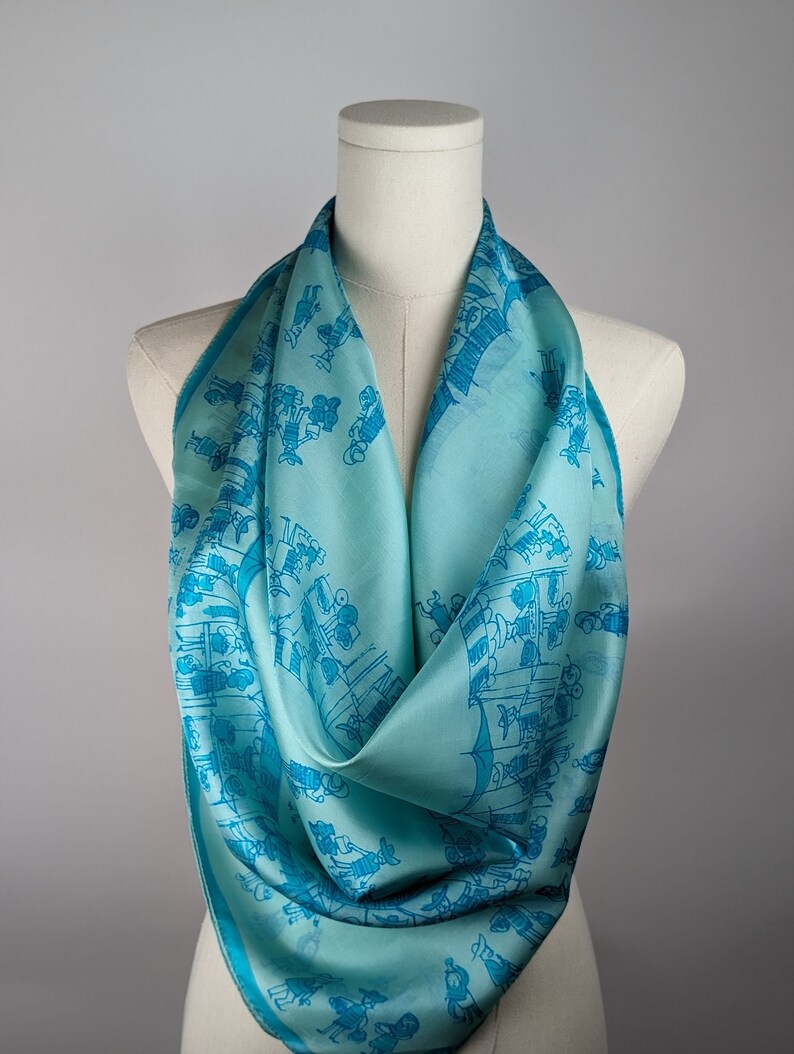 May include: A turquoise blue silk scarf with a repeating pattern of blue figures. The scarf is draped over a white mannequin.