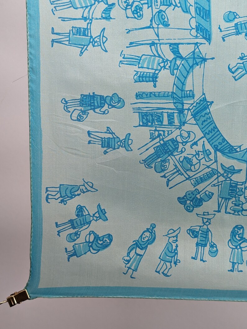 May include: A light blue silk scarf with a white and blue design of people in a market. The design includes people carrying baskets, wearing hats, and holding umbrellas.