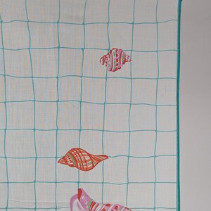 Op de afbeelding: Een wit katoenen zakdoek met een turquoise ruitpatroon en kleurrijke schelpontwerpen. Het zakdoek heeft een turquoise rand en is dubbelgevouwen.