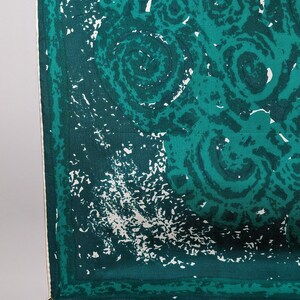 May include: A green and white patterned fabric with a white border. The fabric has a clip attached to the corner.