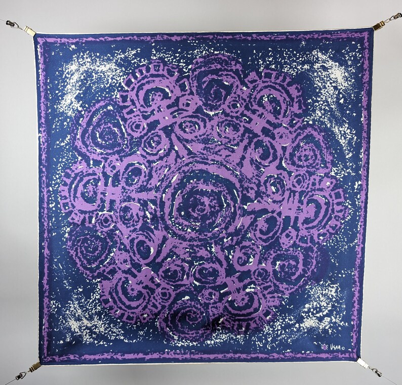 May include: A purple and blue patterned silk scarf with a swirling design. The scarf is hanging from two hooks.