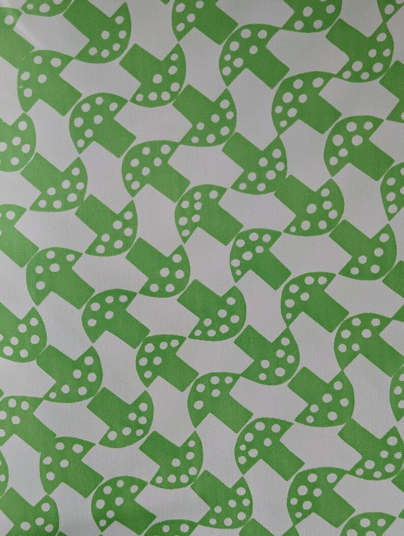 May include: A white fabric with a repeating pattern of green mushrooms. The mushrooms have white dots on them.