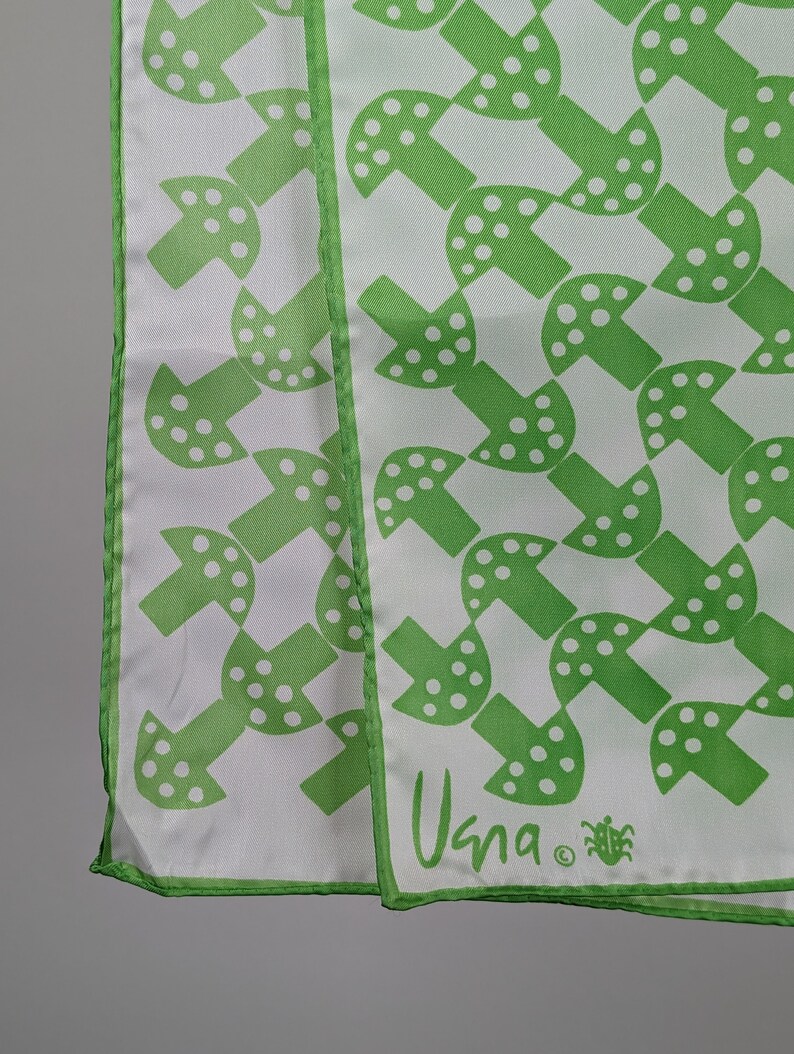 May include: Green and white patterned silk scarf with a white background and green mushroom design. The scarf has a green border and the text "Usna" in green.