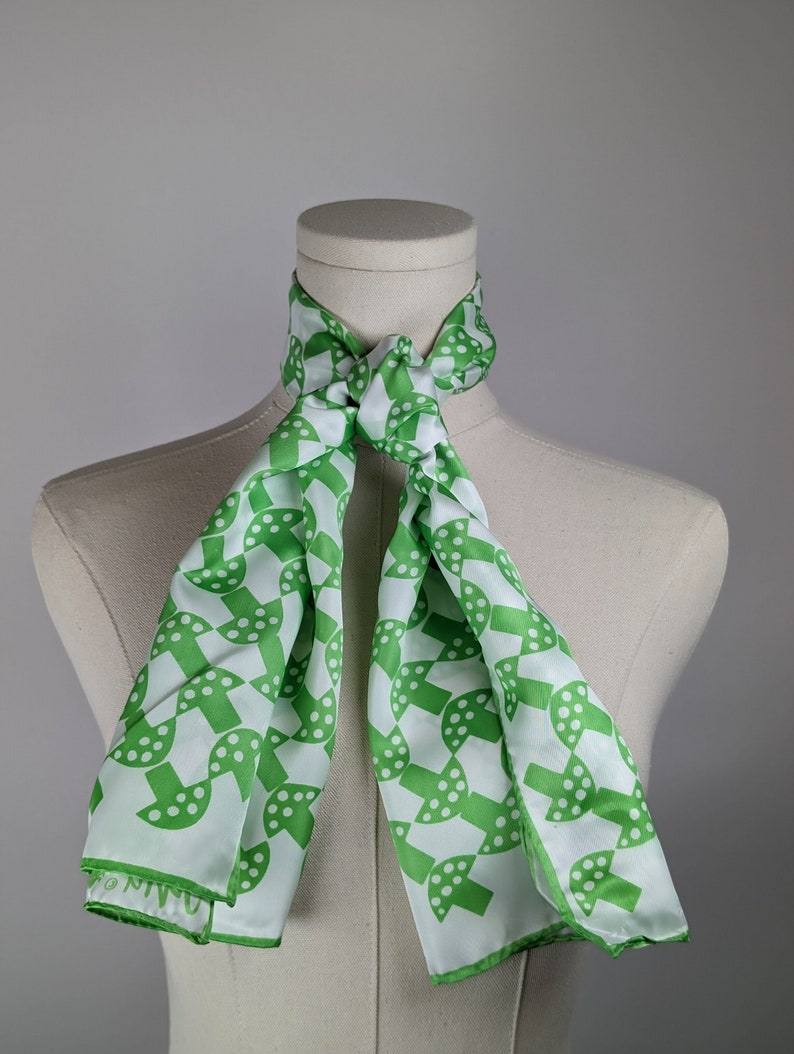 May include: A white silk scarf with a green geometric pattern of circles and dots. The scarf is tied around a white mannequin's neck.