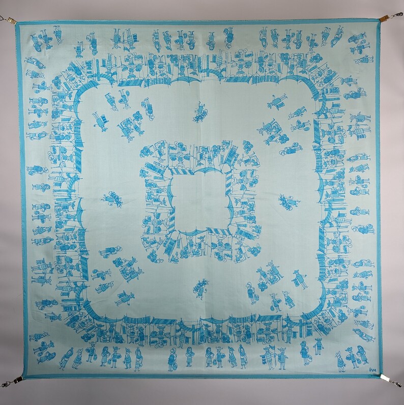 May include: A light blue square tablecloth with a repeating pattern of blue figures and geometric shapes. The figures are arranged in a border around the center of the tablecloth.