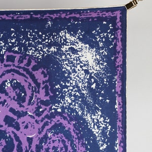 May include: A purple and blue patterned silk scarf with a white border. The scarf is hanging from a gold clip.