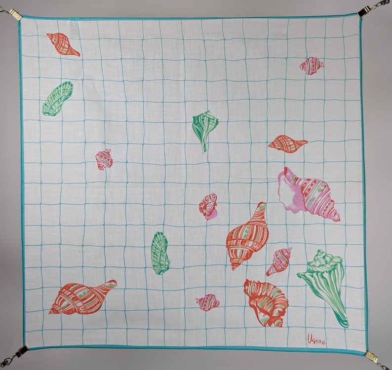 Op de afbeelding: Een witte vierkante katoenen sjaal met een turquoise ruitpatroon en kleurrijke schelpontwerpen. De schelpen zijn in verschillende tinten roze, rood, groen en blauw.