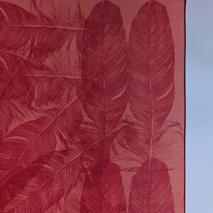 May include: A red silk scarf with a pattern of white feathers. The scarf is hanging from a hook.
