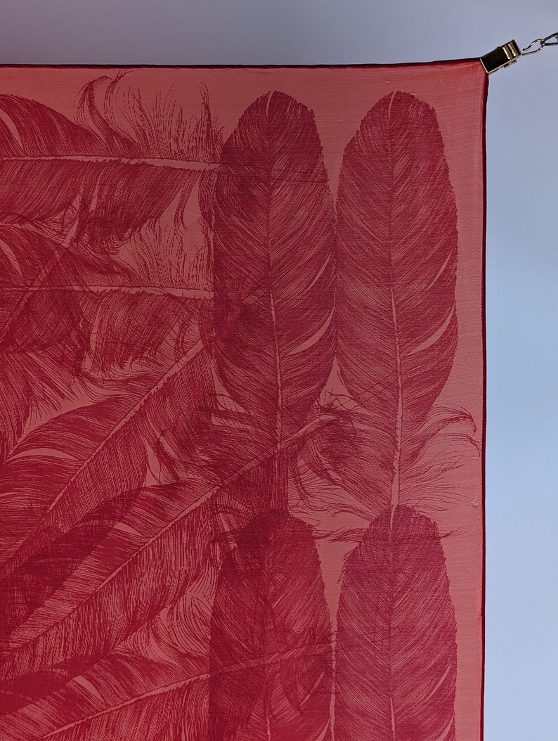 May include: A red silk scarf with a pattern of white feathers. The scarf is hanging from a hook.